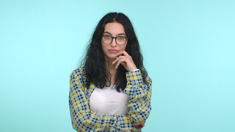 Attractive skeptical woman takes-off glasses, nod while listening, shake head doubtful and unamused, raise eyebrow in disbelief and look away, standing over blue background.