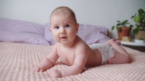 A cute funny newborn baby smiling at the camera lies on his stomach on the bed at home. Beautiful playful Caucasian child. Slow motion 4K video