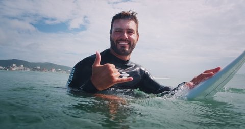 FLORIANOPOLIS, BRAZIL - MARCH, 2021: Brazilian surfer smiles and shows the Shaka sigh. Campeche beach, Brazil