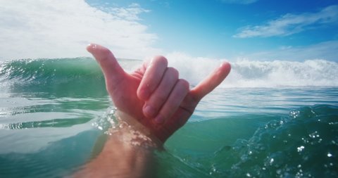 Surfer shows the Shaka sign in front of the braking wave