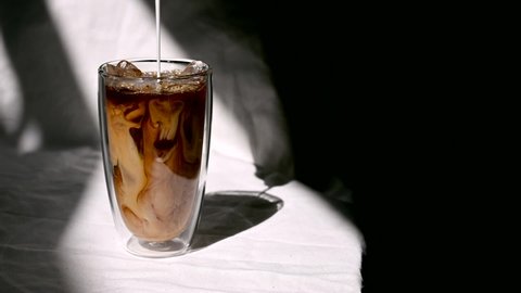 Barista pouring milk into a glass of iced coffee