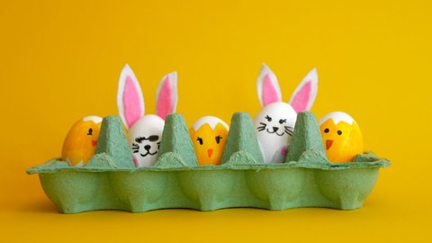 Empty egg carton fills in with painted eggs, bunnies and chicks on the yellow background. An egg appears in the center with the inscription happy easter. Stop motion animation.