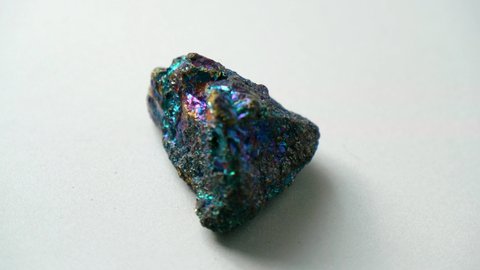 Natural multi-colored green blue chalcopyrite stone spins around its axis on a white stand and white background. Gems, minerals, collection of natural stones, close-ups, study of minerals