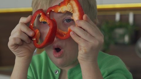 Sweet happy boy with Down Syndrome cooking salad and having fun in the kitchen with vegetables. Close-up