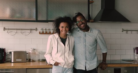 Happy young family african wife, husband with dreadlocks pleased good-looking 35s couple standing in domestic modern comfort remodelled kitchen smiling looking at camera. Homeowners portrait concept