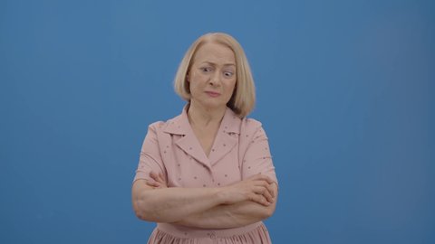 Angry, aggressive, panicked old woman. Studio shot isolated on blue background.