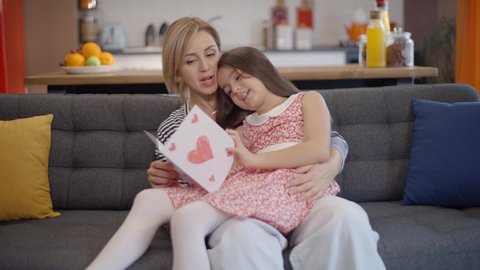 Happy mother's day! The little girl congratulates the mother and gives a heart postcard. The mother and daughter are smiling and hugging. Slow motion video.