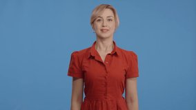 Young woman pointing with his finger at the advertising space at the top of the screen. Indoor studio shot isolated on blue background. Slow motion video.