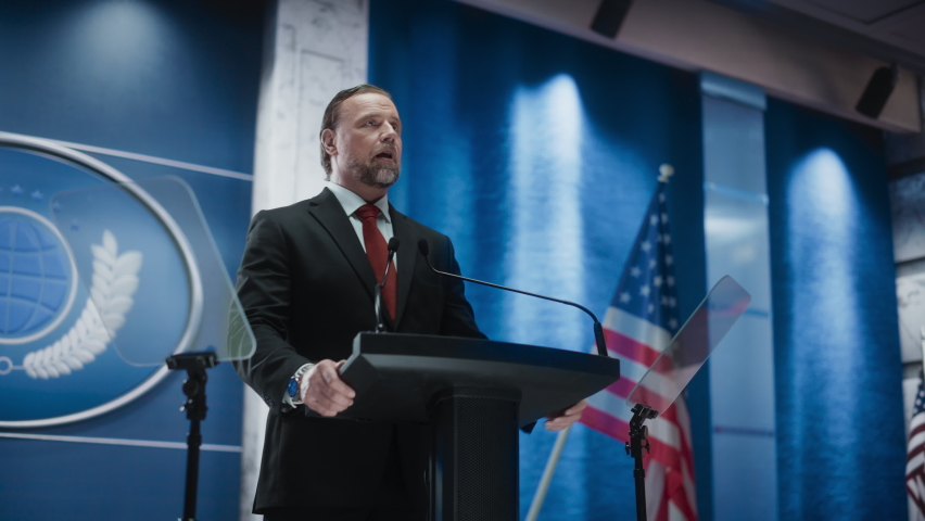 Charismatic Organization Representative Speaking at a Press Conference in Government Building. Press Officer Delivering a Speech at a Summit. Minister at Congress. Backdrop with American Flags. | Shutterstock HD Video #1068497864
