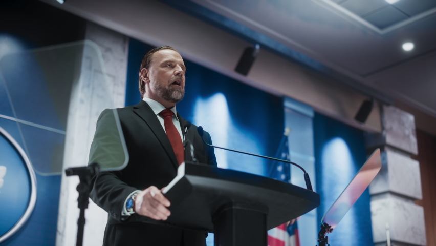 Portrait of Organization Representative Speaking at a Press Conference in Government Building. Press Officer Delivering a Speech at a Summit. Minister at Congress. Backdrop with American Flags. | Shutterstock HD Video #1068497885