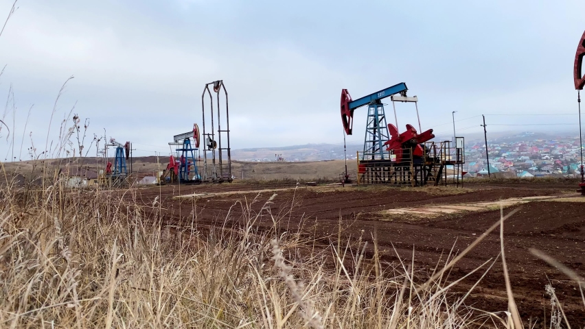 Three machines for pumping oil and gas. Silhouette of working oil pumps from a field in a foggy field against the background of grass and an industrial city. Equipment for oil and gas fields.
