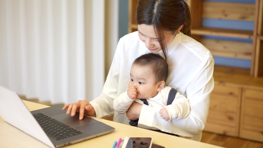 A woman holding a baby and operating a laptop Royalty-Free Stock Footage #1068500531