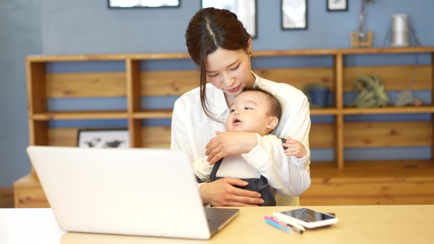 A woman holding a baby and operating a laptop Royalty-Free Stock Footage #1068500537