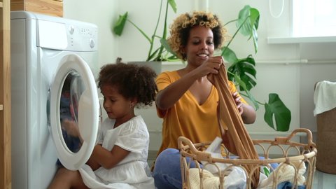 black afro woman and daughter load modern washing machine with dirty laundry. Spbd two people mother and kid wash clothes. concept help, together, housekeeping.