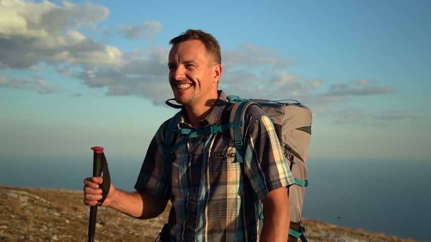portrait of man hiker as he walk with trekking poles outdoors on setting sun. Spbd mountain hike travel climbing on black sea crimea background. male tourist enjoy front view, smile