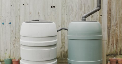 Rainwater stored in two large water barrels in the backyard, filling a green watering can to water plants