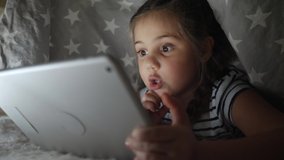 little girl under the blanket with digital tablet. kid dream online video games at night concept. daughter kid watching online video under the covers with digital tablet network. child on social media