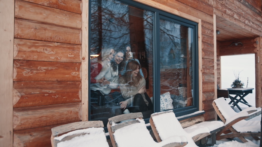 Women, best friends having fun winter holidays in wooden mountain house. Drinking hot beverages and gossiping near the big window. High quality 4k footage