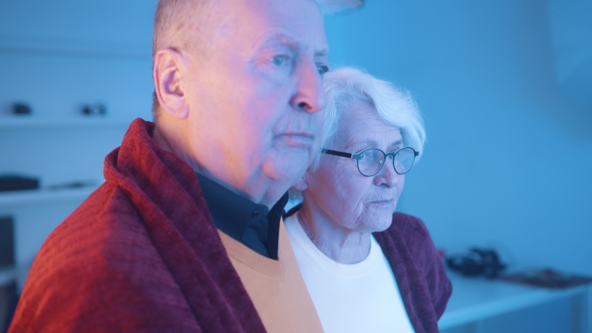 Elderly couple looking through the window with flashing police lights. Taking step back in fear. High quality 4k footage