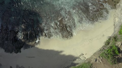 Aerial reversing over a cliffside beach and tilting up to reveal a natural rock arch bridge formation spanning a beautiful ocean bay with a woman walking to the edge of the cliff to admire the view