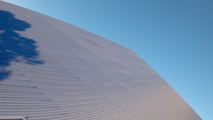Aerial moving up and around the side of the Walter Pyramid at Long Beach State University under a bright sunny blue sky with shadows and the distant city along the horizon