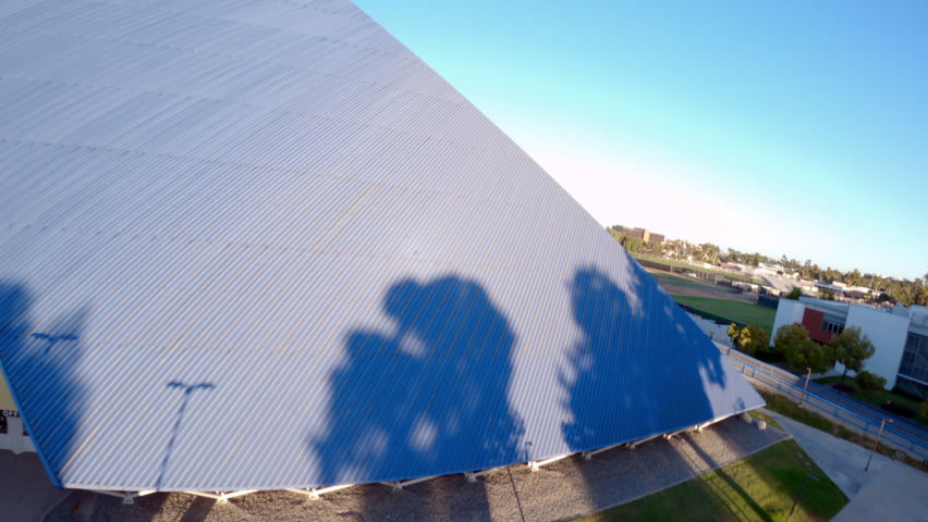 Aerial moving forward and up the side of the Walter Pyramid at Long Beach State University under a bright sunny blue sky with shadows and the distant city along the horizon