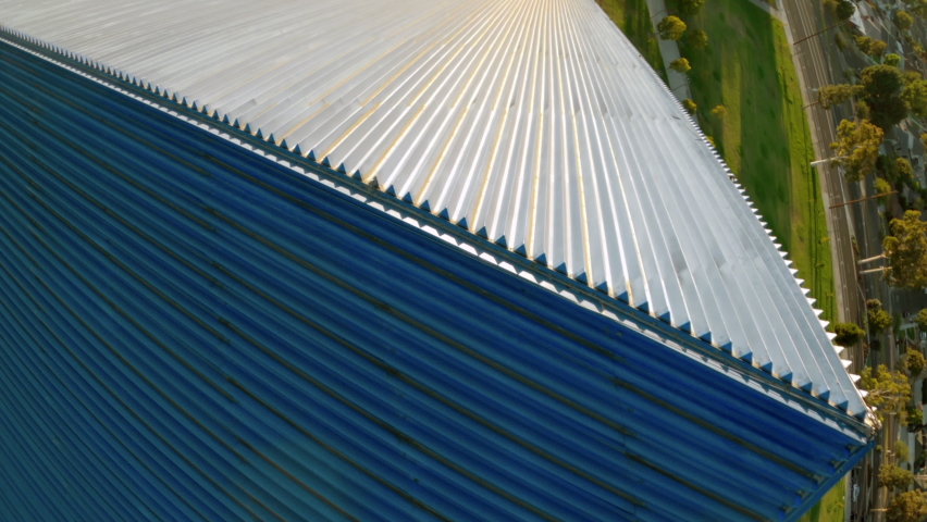 Aerial quickly moving forward down the side of the Walter Pyramid at Long Beach State University under a bright sunny blue sky with shadows and the distant city along the horizon