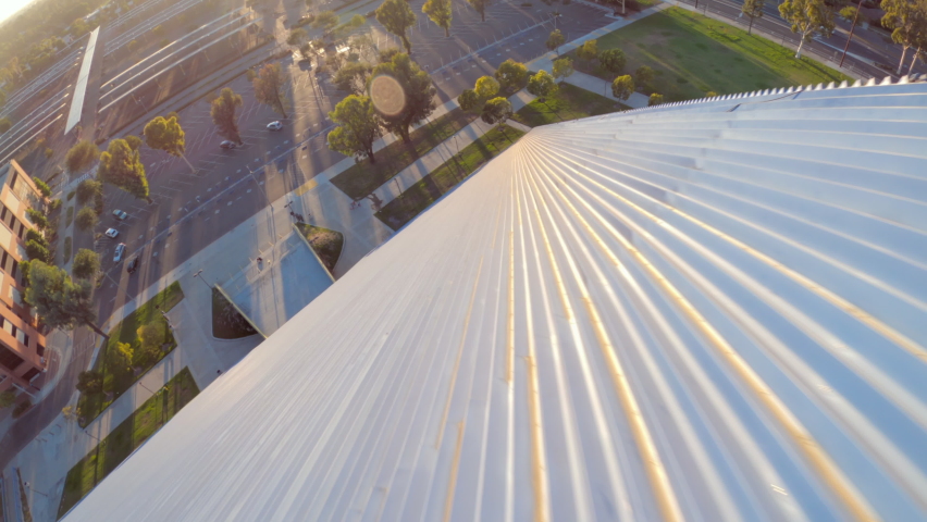Aerial quickly moving forward down the side of the Walter Pyramid at Long Beach State University under a bright sunny blue sky with shadows and campus buildings in the background