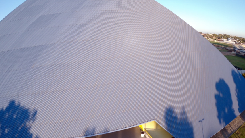 Aerial moving forward and up the side of the Walter Pyramid at Long Beach State University under a bright sunny blue sky with shadows and the distant city along the horizon