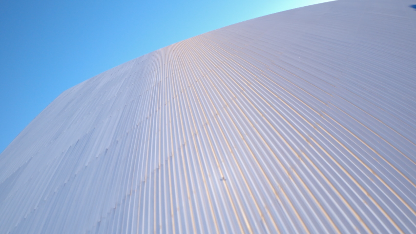 Aerial quickly moving forward and up the side of the Walter Pyramid at Long Beach State University under a bright sunny blue sky with shadows and the distant city along the horizon