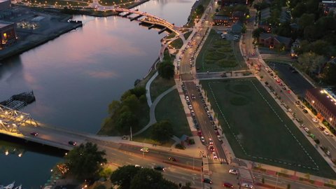 Aerial shot of people on bridge over river in city at dusk, drone flying forward over structures - Providence, Rhode Island