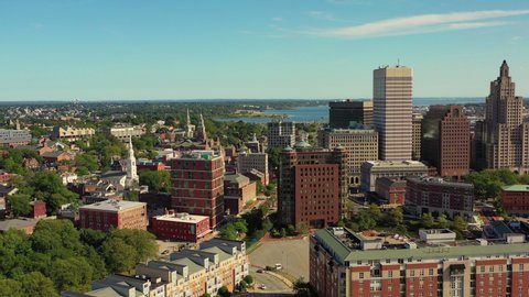 Aerial shot of buildings in city with river against blue sky, drone flying backward over cityscape on sunny day - Providence, Rhode Island
