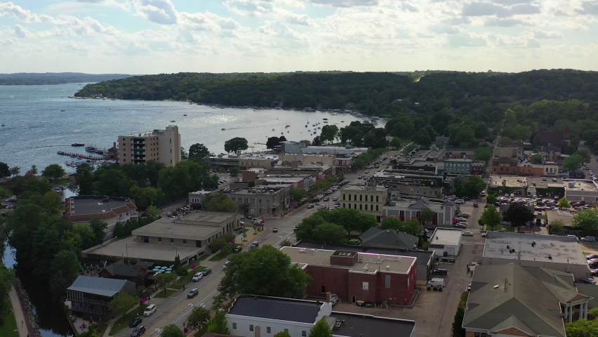 Aerial shot of vehicles on street amidst buildings in city, drone flying forward towards harbor on lake against sky - Lake Geneva, Wisconsin