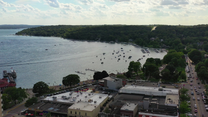 Aerial shot of vehicles on street amidst buildings in city, drone flying backward from harbor on lake against sky - Lake Geneva, Wisconsin