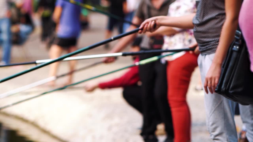 Hands of men and women holding fishing rods while standing on bank of river, blurred background. Partial view of people enjoying fishing in summer. Concept of hobby
