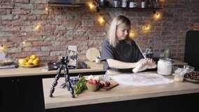 professional culinary blogger performs homemade cakes preparation process kneading dough and sprinkle with flour while record video on black smartphone on foreground