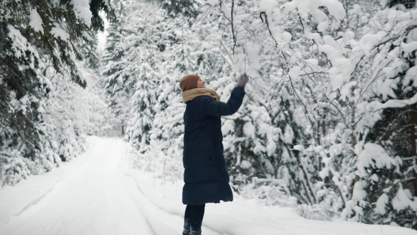 Young woman shakes off the snow from the tree in winter forest. She smiles and goes forward. High quality 4k footage