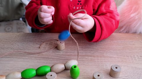 small child, toddler stringing colored wooden beads on a string, children's fingers close-up, concept of development of fine motor skills, tactile sensations, creativity, children's entertainment