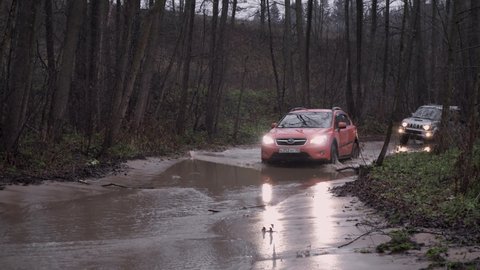 Dmitrov, Russia - CIRCA 2020: Subaru XV and Suzuki Jimny suv with headlights driving through large muddy puddle offroad