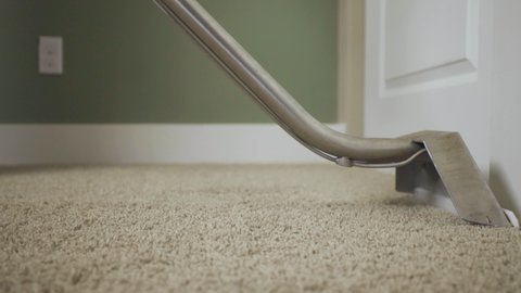 Worker cleaning carpet using professional-grade equipment for steam cleaning hot water extraction of carpet fibers. In bedroom or residential office. Still shot with slow wand stroke, 50% speed.