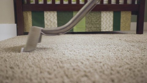 Worker cleaning carpet using professional-grade equipment for steam cleaning hot water extraction of carpet fibers. In Baby or Kid's bedroom. Mid shot, pan, wand head, 50% speed.