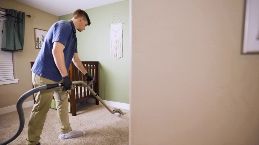 Man cleaning carpet using professional-grade equipment for steam cleaning hot water extraction of carpet fibers. In Baby or Kid's bedroom. Wide, pan, behind wall to reveal man, 50% speed. Royalty-Free Stock Footage #1068522719