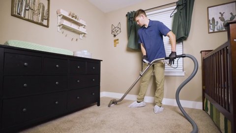 Man cleaning carpet using professional-grade equipment for steam cleaning hot water extraction of carpet fibers. In Baby or Kid's bedroom. Wide, pan, man to crib, 50% speed.