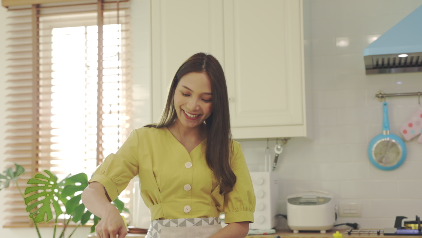 A beautiful Asian girl makes breakfast by looking at how to make it with her laptop computer with a happy face. At her own house