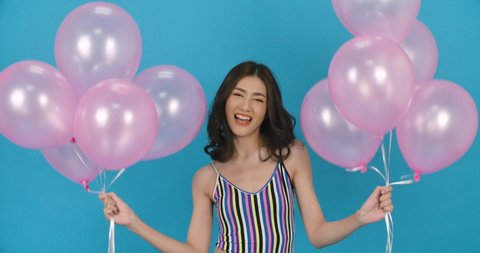 Portrait of young beautiful asian woman holding balloon in hand  with attractive smile in blue background. Pretty girl dance and look to camera with happy emotion. Fashion, travel and beauty concept.