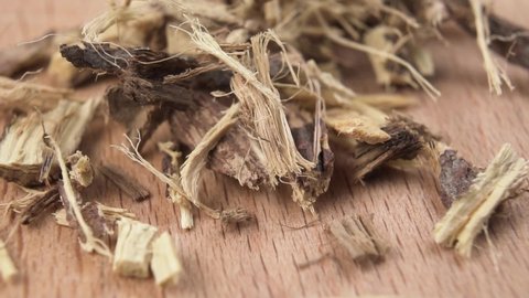 Dried chopped licorice root falls in slow motion onto a wooden surface. Herbal medicine concept. Glycyrrhiza glabra