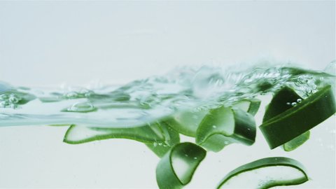 Pieces of aloe are floating in the water. Aloe vera in water. Air bubbles. Advertising concept. Natural cosmetics production. Aloe Vera Gel. White background. Slow motion.
