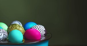 Close-up video of colorful Easter eggs on rotating plate on green background with copy space