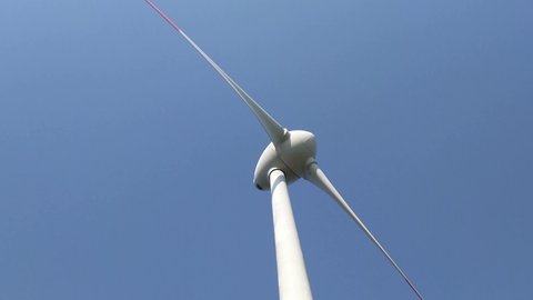 Wind turbine power generator spinning in the wind. Low angle view of spinning white sustainable electricity generator on blue sky background