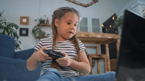Happy girl playing video games with a joystick. Child gambling addiction. Happy little girl playing video game home. Concept of child gambling addiction. Happy little girl learning to work on laptop